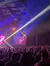 A performer is suspended upside down on stage, illuminated by vibrant spotlights, in front of a large audience.