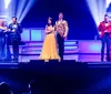 A group of performers on stage dressed in colorful costumes are energetically engaged in a lively act with one holding a sign that reads How to Succeed in Branson Shows