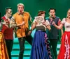 A group of performers on stage dressed in colorful costumes are energetically engaged in a lively act with one holding a sign that reads How to Succeed in Branson Shows