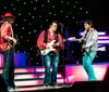A performer dressed in a red and black patterned outfit and hat is on stage under colorful lights gesturing expressively