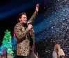 Three people are performing on stage energetically dancing and wearing colorful hoodies and festive pants
