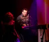 Three musicians are performing on stage with guitars under colorful stage lighting