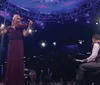 A woman is playing the violin on stage next to a man at a grand piano with a backdrop of snowflake decorations and dramatic lighting