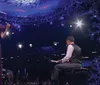 A woman is playing the violin on stage next to a man at a grand piano with a backdrop of snowflake decorations and dramatic lighting