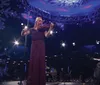A woman is playing the violin on stage next to a man at a grand piano with a backdrop of snowflake decorations and dramatic lighting