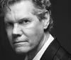 A person is singing into a microphone while playing a guitar with the name Randy Travis displayed at the bottom