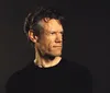 A person is singing into a microphone while playing a guitar with the name Randy Travis displayed at the bottom