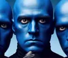 Three individuals with blue-painted faces and intense expressions are closely grouped together against a blue background