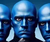 Three individuals with blue-painted faces and intense expressions are closely grouped together against a blue background