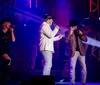The image shows a lively stage performance by Bransons Famous Baldknobbers featuring colorful lighting and musicians with an inset displaying an entertainer in vibrant attire