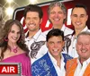 This image features a group of eight smiling people in colorful clothing posed together with an As Seen on TV graphic suggesting they might be part of a television show or advertisement