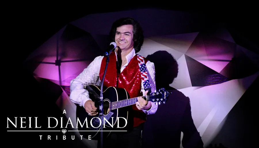 A performer in a sparkly red vest and white shirt is playing a guitar on stage under the banner A Neil Diamond Tribute.