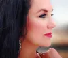 The image shows a close-up profile of a woman with dark hair pink lipstick and prominent eye makeup gazing off to the side against a blurred background