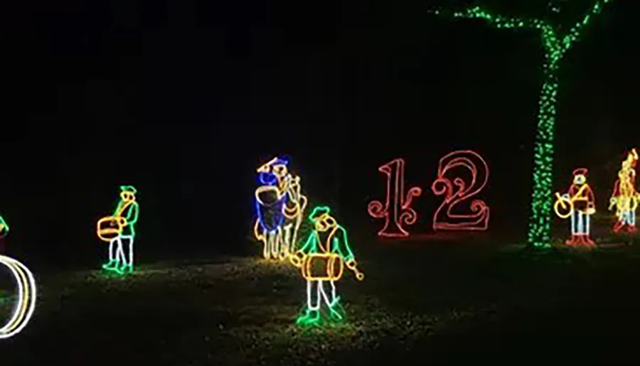 The image shows a festive outdoor light display featuring animated figures playing drums and the numbers 12 illuminated against a dark background.