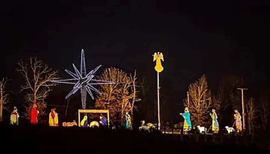 A nighttime nativity scene is illuminated with colorful figures, a large star, and an angel on a pole.
