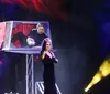 A stage performer and magician are posing in front of a dramatic backdrop with colorful smoke effects while an inset shows a plated meal and glasses on a table
