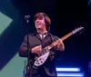 A musician dressed in a colorful vintage-style costume is performing on stage with a guitar