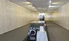 An empty room with track lighting features a small memorial setup, including a table with a white cloth, a plate, an American flag, a rose, and a POW/MIA chair.