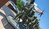 The image shows a bronze statue of soldiers in a marching formation, with a model airplane on display above them, at the entrance of a brick building under a clear blue sky.