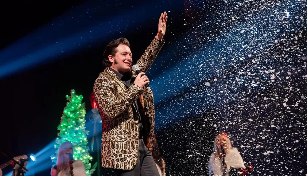 A performer in a leopard print jacket sings on stage amidst falling snowflakes with festive lights and decorations in the background