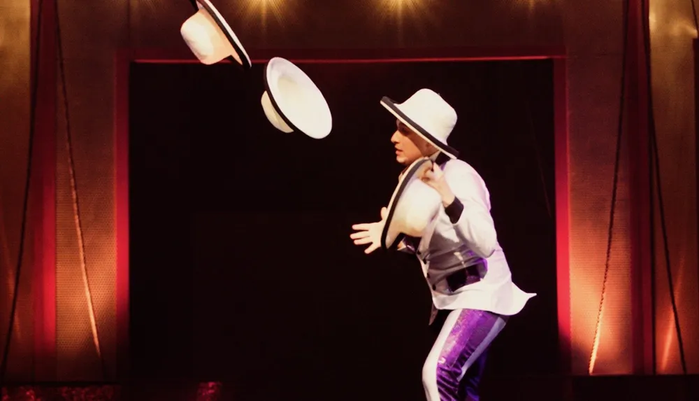 A performer in a white hat and costume is catching flying hats on stage creating a dynamic and entertaining visual spectacle