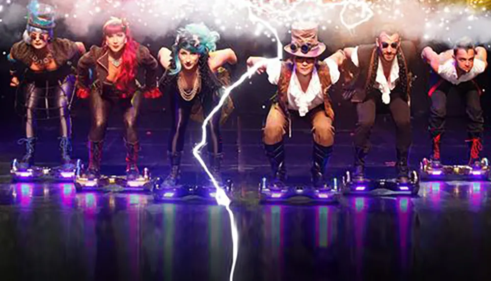 A group of performers in steampunk-inspired costumes are hovering with their hands connected by a simulated bolt of electricity on a smoke-filled stage illuminated by purple lights