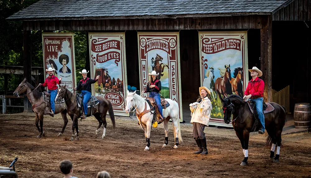 The image captures a theatrical Wild West show with performers on horseback and in period costumes set against a backdrop of colorful stage posters