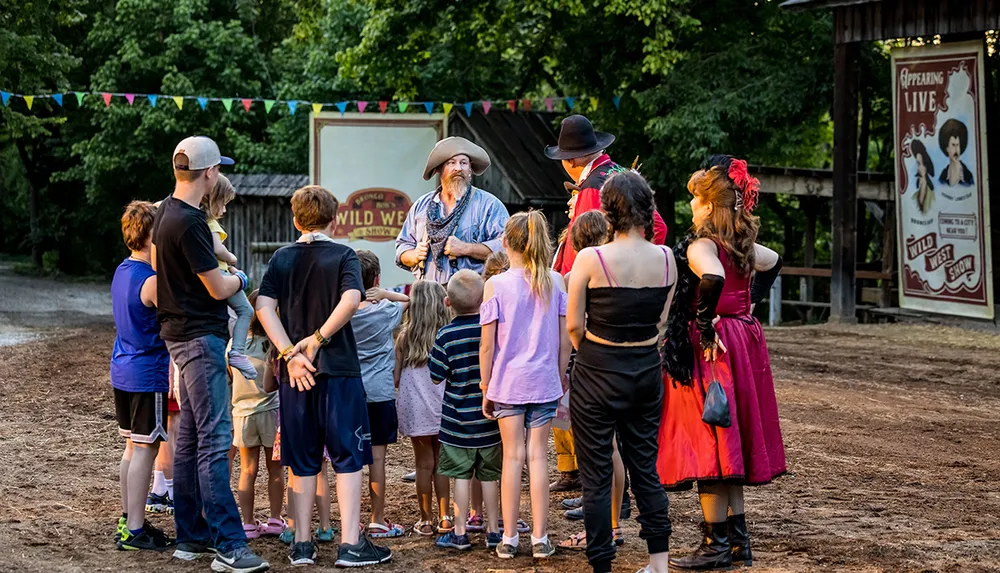 A group of individuals including children and adults dressed in Wild West attire gather outdoors for what appears to be an interactive event or performance