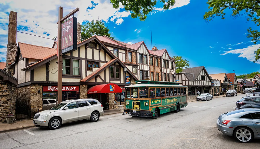 A quaint street scene featuring Tudor-style architecture with a trolley tour bus and vehicles parked alongside the buildings under a clear blue sky