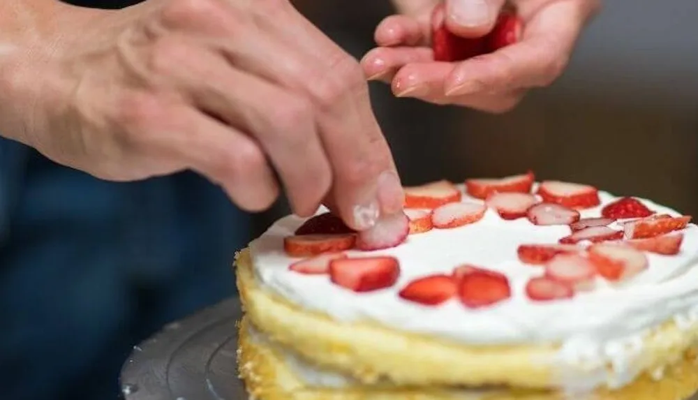A person is decorating a cake with sliced strawberries
