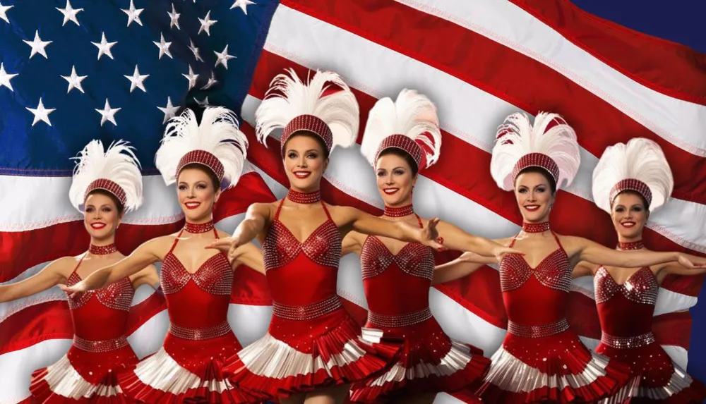 A group of dancers in red costumes with feathered headpieces poses in front of the American flag