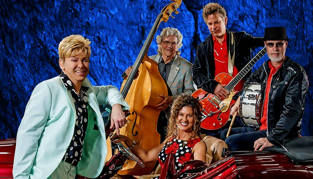 A group of five musicians poses with their instruments in front of a blue textured background