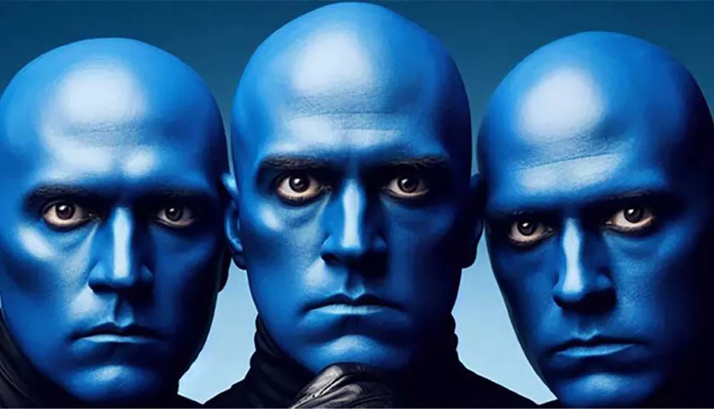 Three individuals with blue-painted faces and intense expressions are closely grouped together against a blue background