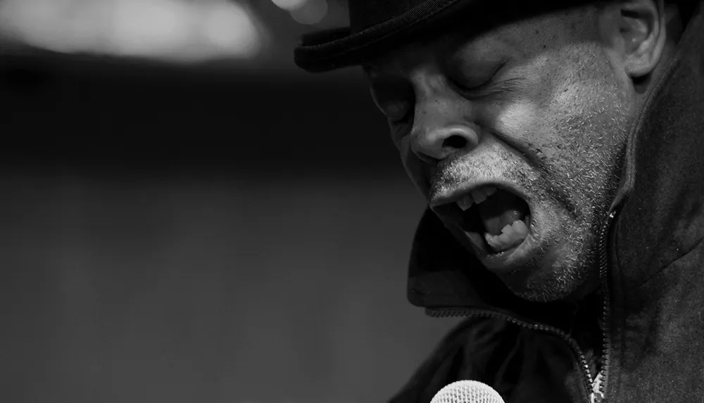 A person wearing a hat passionately sings into a microphone