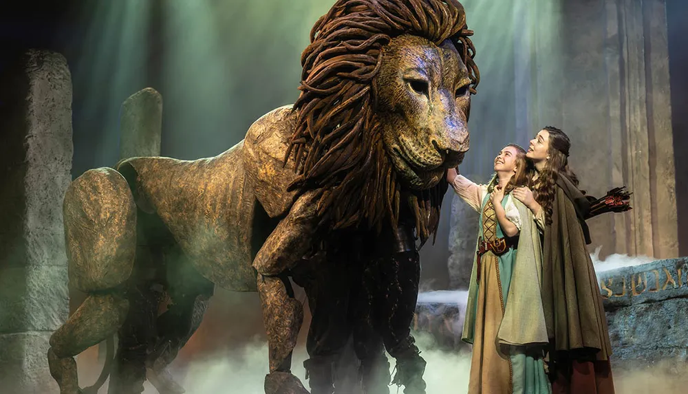 Two people in medieval-style costumes interact with a large lion puppet on a theatrical stage filled with mist and dramatic lighting