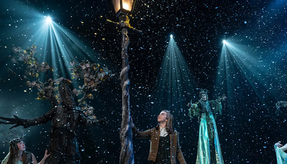 A person stands under a lamppost in a snowy magical scene with costumed figures and dramatic lighting