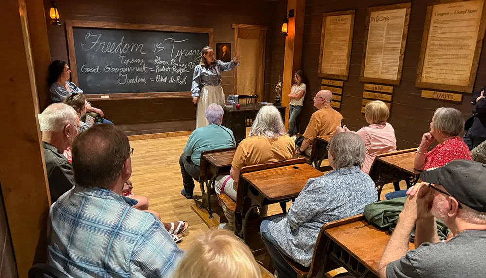 A person is giving a lecture about Freedom vs Tyranny to an attentive audience in a classroom setting with historical documents displayed on the walls