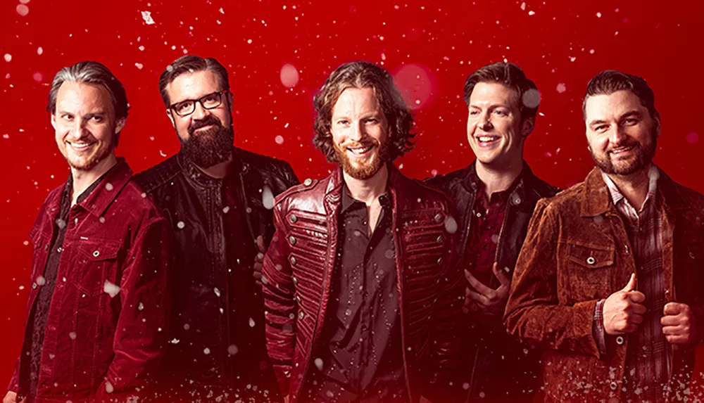 Five men wearing jackets are smiling against a festive red backdrop with snowflakes