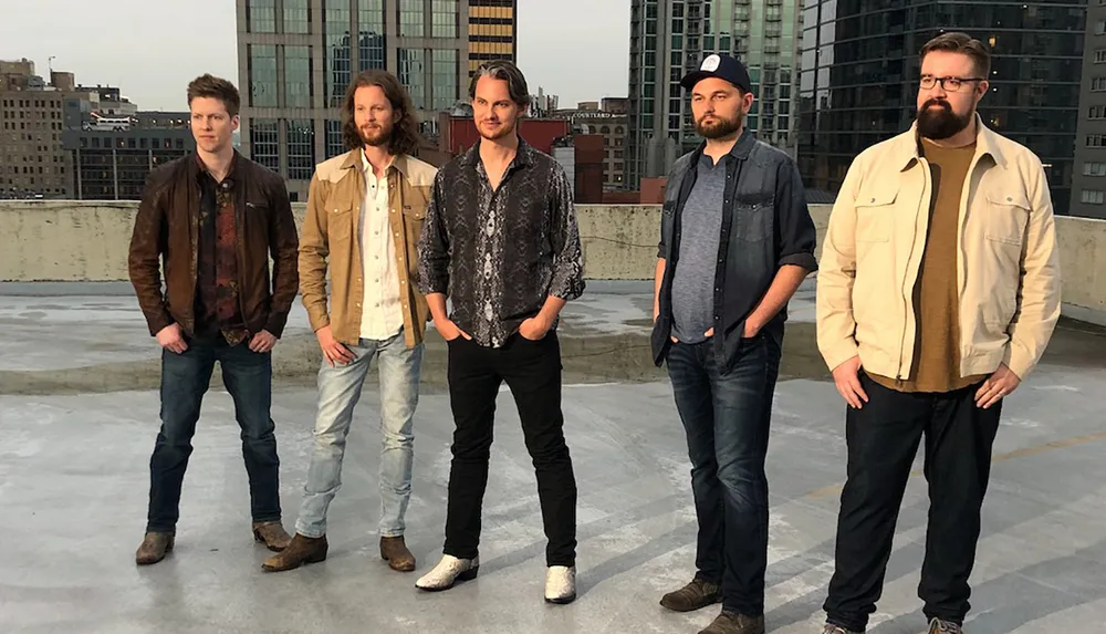 Five men are standing on a rooftop in front of a city skyline