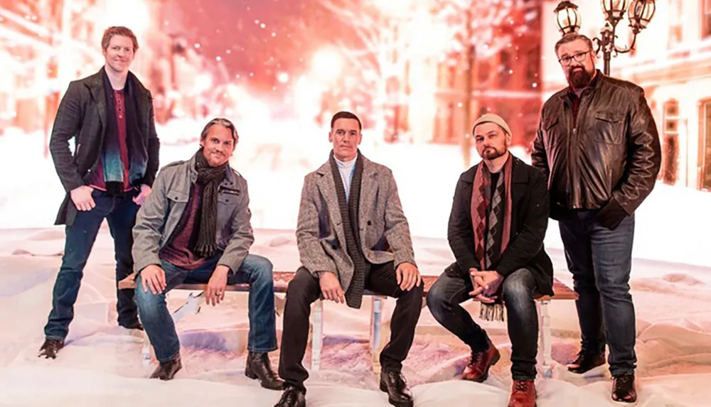 Five men in winter clothing are posing against a festive snowy backdrop