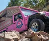 A pink Jeep is navigating a rocky off-road terrain amidst trees and rough slopes