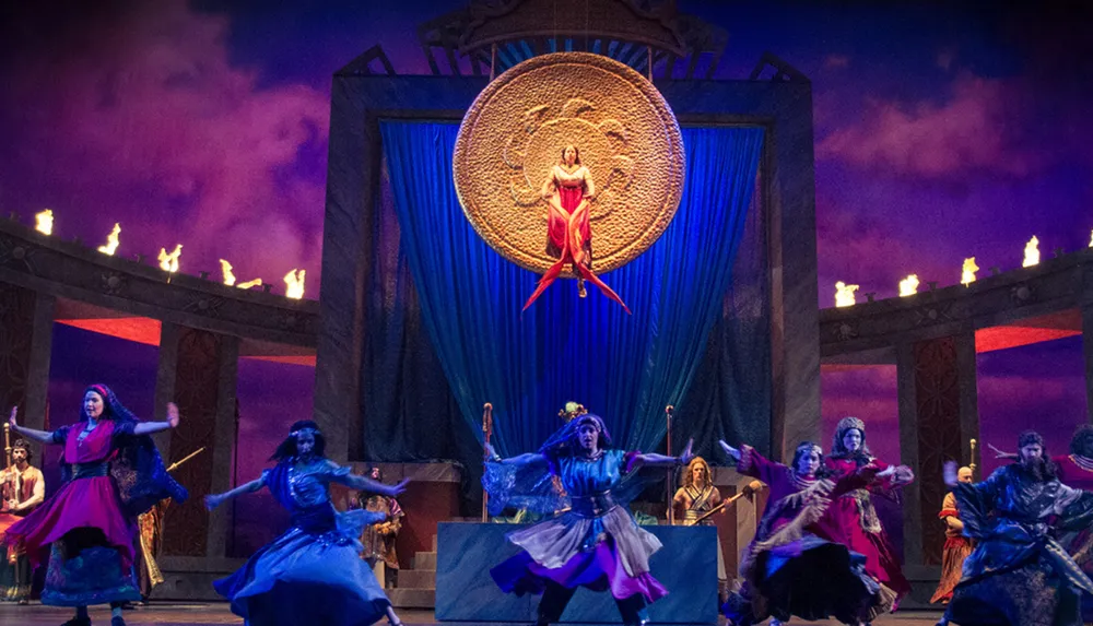 Performers are participating in a dramatic and vibrant stage production with dynamic dance movements under atmospheric lighting