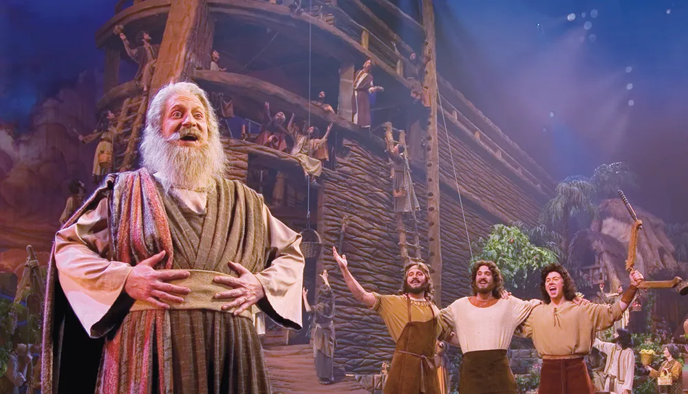 A group of performers on a stage appear to be in a scene from a theatrical production with an elaborate set that includes a large ship and a fantastical backdrop