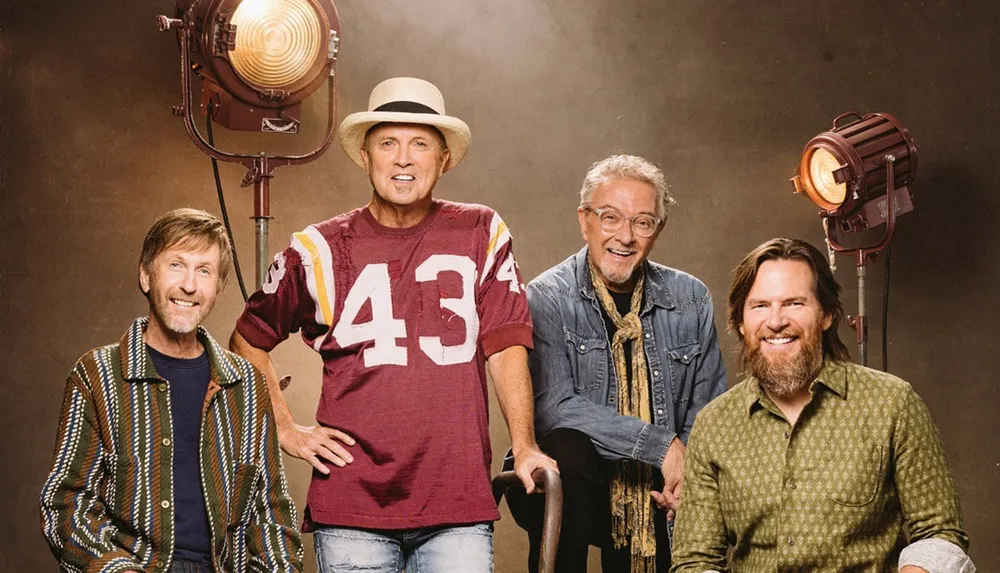 Four men are posing together in front of studio lights with one wearing a hat and jersey