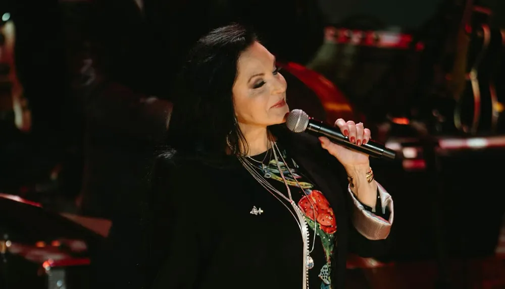 A woman is singing into a microphone with her eyes closed conveying an emotional performance