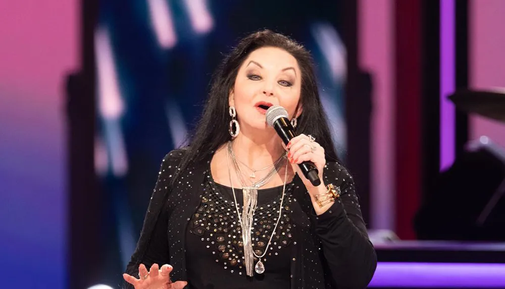 A woman is performing on stage singing into a microphone with a colorful background